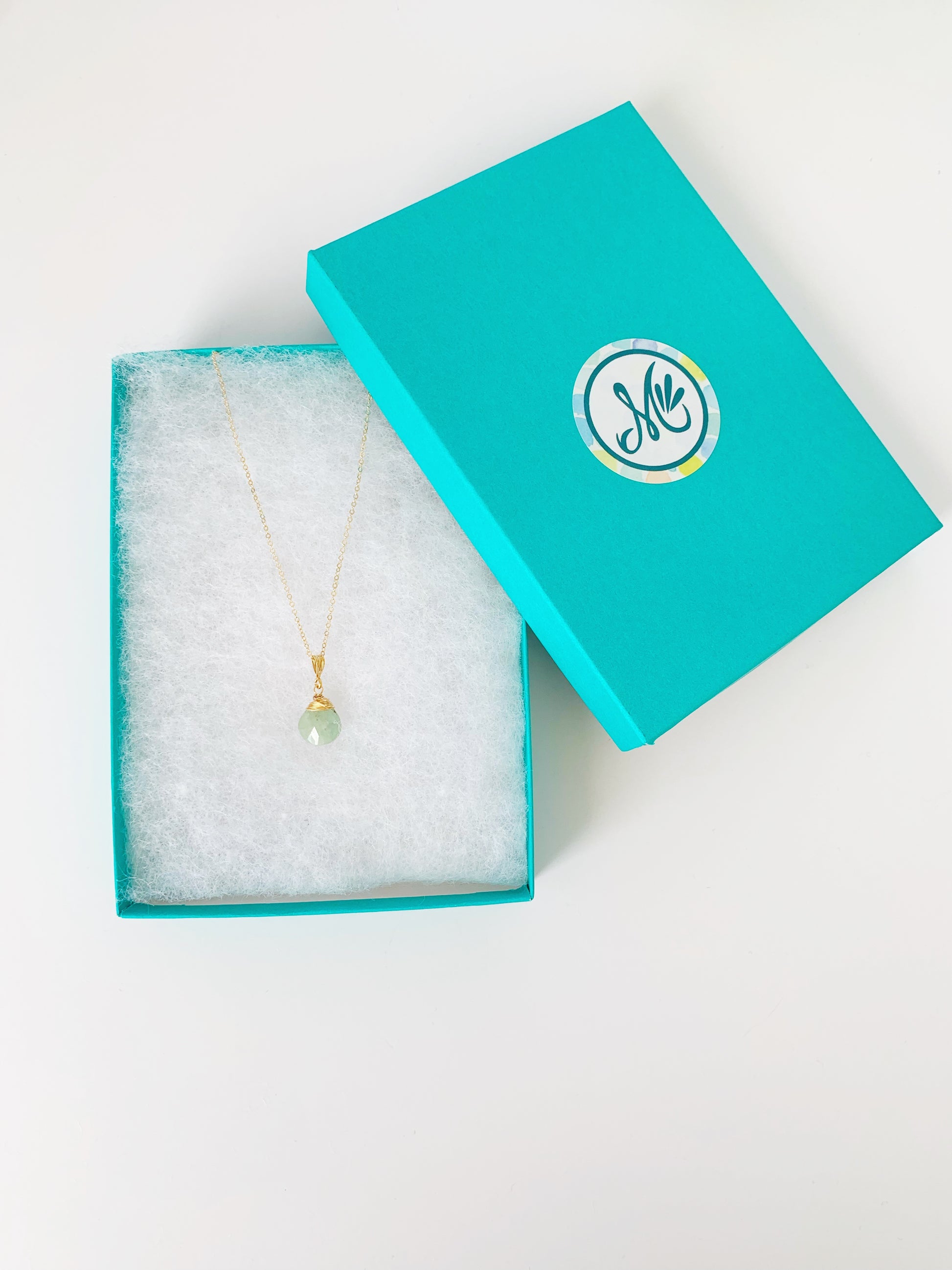 Raindrop necklace in 14k gold filled with aquamarine is pictured here in a teal gift box on a white surface