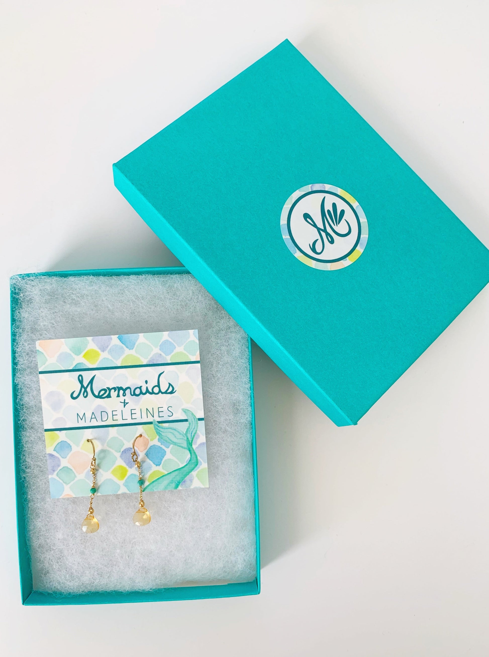 Ray of sunshine earrings photographed in a teal gift box on a white surface