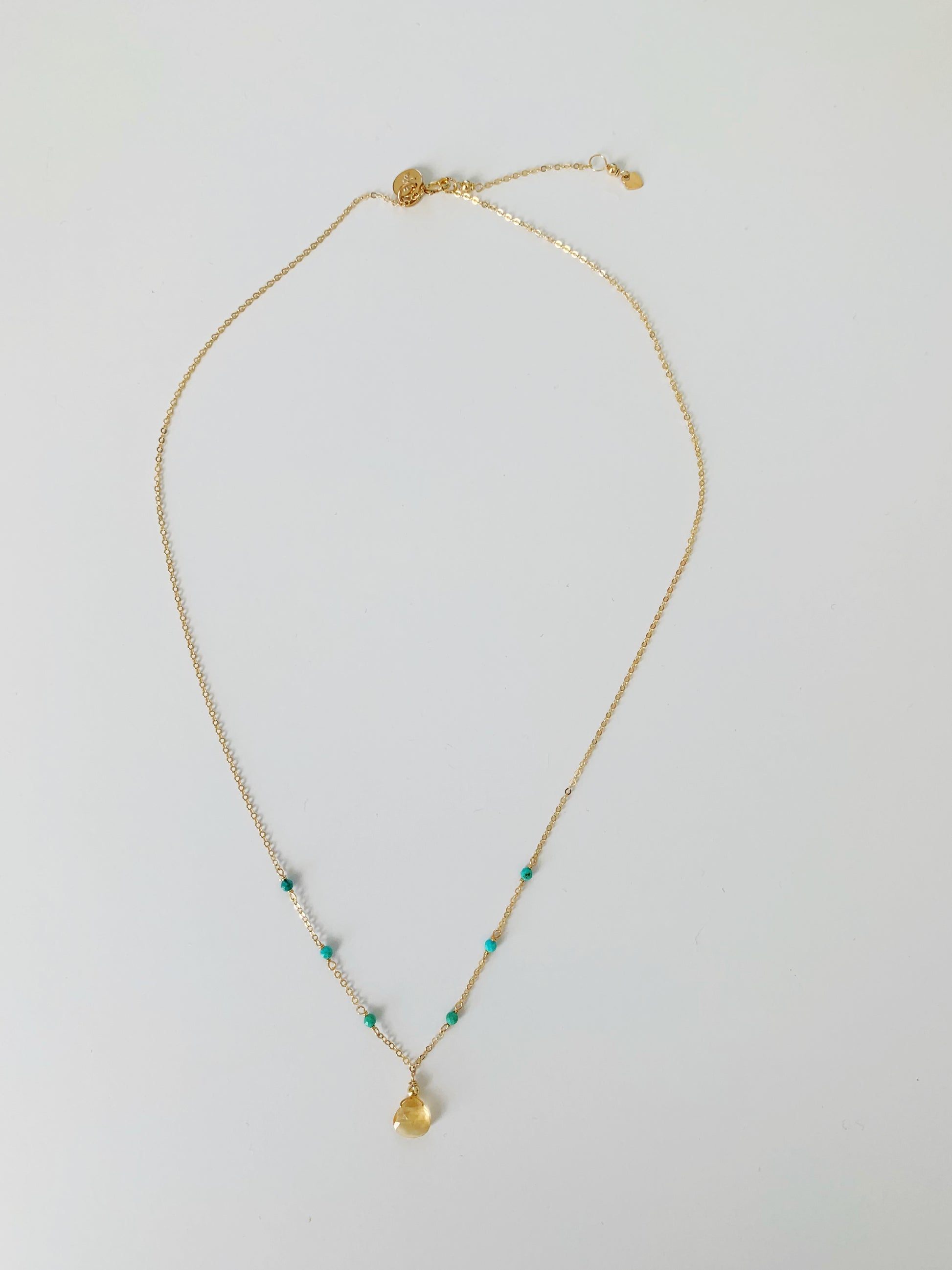 Ray of Sunshine necklace by mermaids and madeleines as a citrine drop at the center with natural turquoise beads on 14k gold filled chain. This is an image of the full length of the necklace and pictured on a white surface