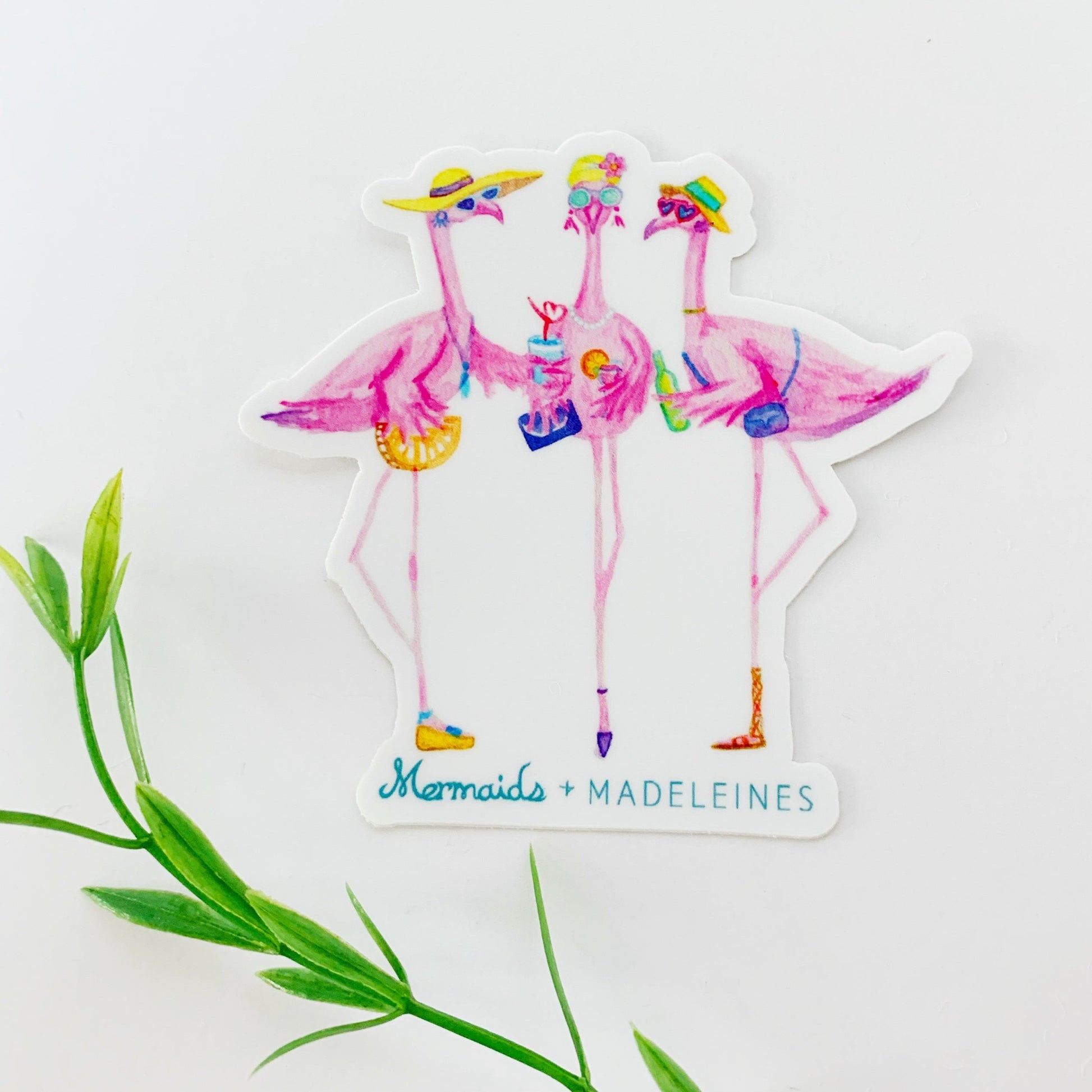 The flamingal sticker is created from original artwork made with acrylic paint and marker its 3 flamingo ladies dressed in summer hats and various footwear. This is a picture of a sticker on a white background with blurred greenery along the bottom of the picture