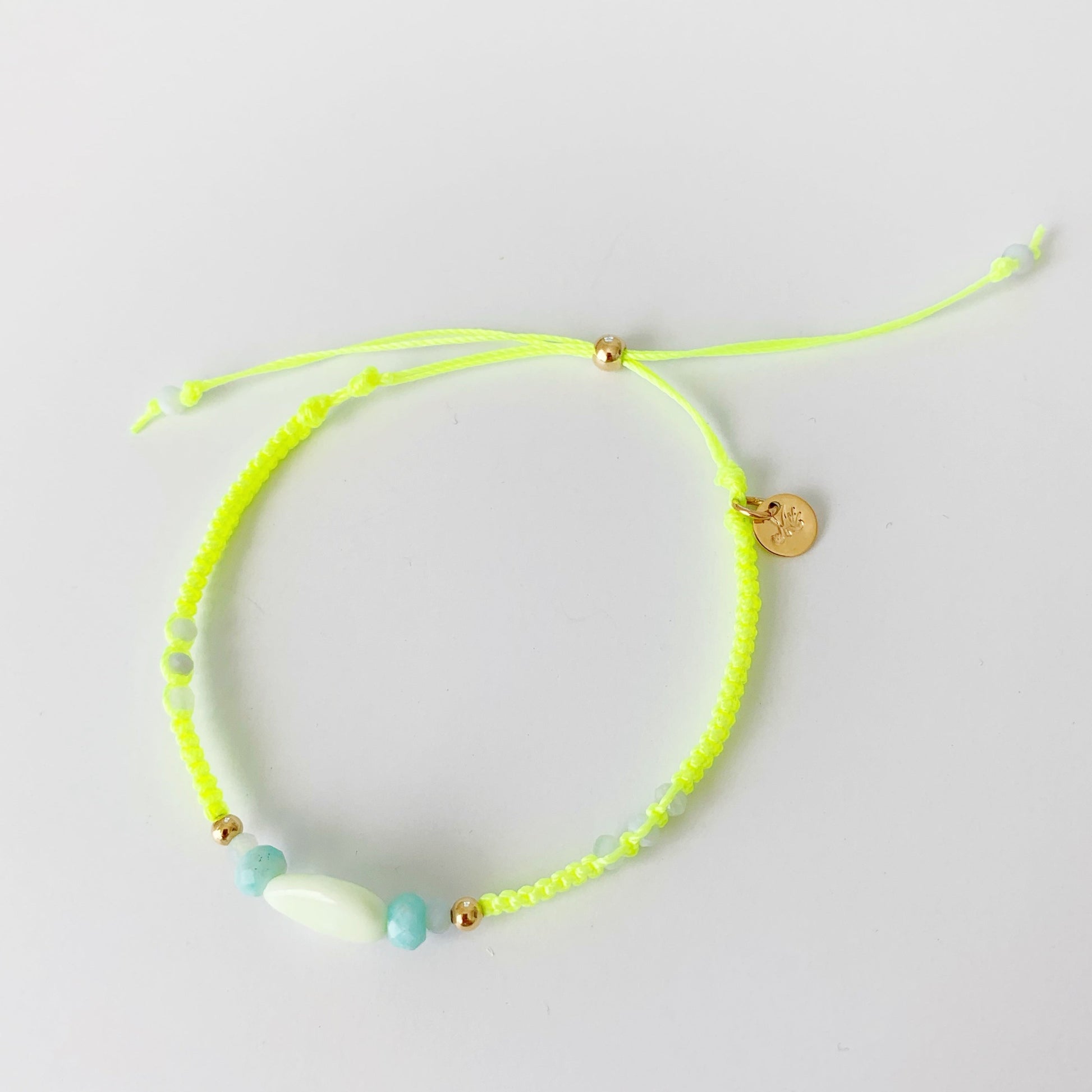 a top view of the neon yellow macrame friendship bracelet by mermaids and madeleines pictured on a white surface