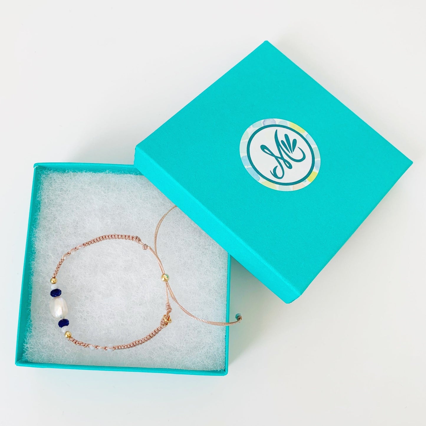 Tan macrame adjustable friendship bracelet pictured in a teal mermaids and madeleines gift box photographed on a white surface
