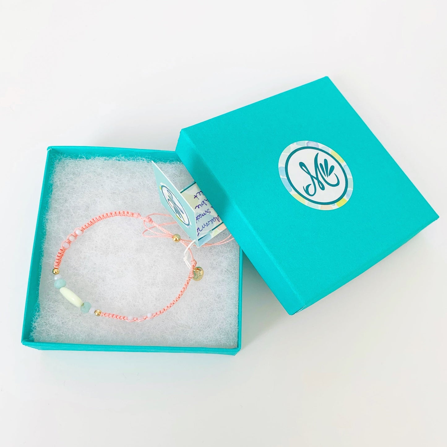 peach macrame friendship bracelet pictured in a teal mermaids and madeleines gift box on a white background