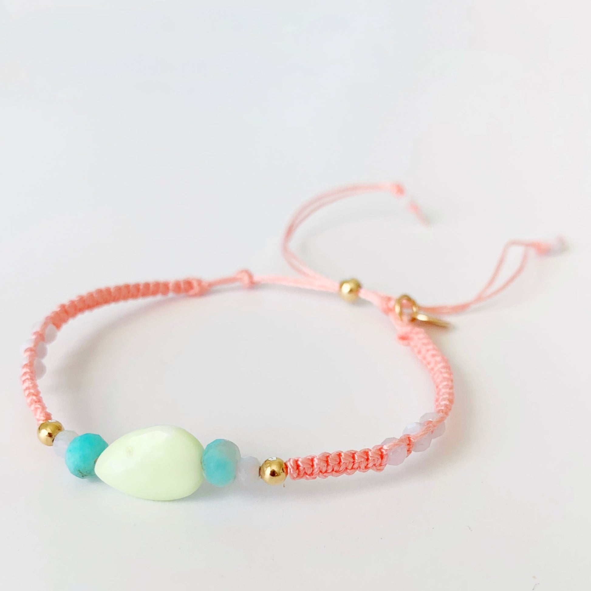 Mermaids and madeleines captiva macrame bracelet in color peach tropical smoothie features semiprecious beads at the center and 14k gold filled slide bead clasp. this bracelet is pictured on a white background